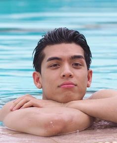 a young man is sitting in the water with his arms crossed and looking at the camera