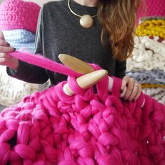 a woman sitting on a bed holding a pink knitted blanket with a wooden spoon in it