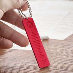 a hand holding a red piece of metal with a chain attached to it on top of a wooden table