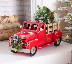 an old red truck with a christmas tree in the back is sitting on a mantle