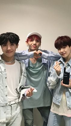 three young men standing next to each other in front of a white wall holding up their cell phones