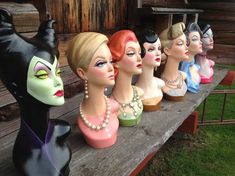 a row of mannequin heads sitting on top of a wooden bench