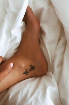 a person laying on top of a bed covered in white sheets with tattoos on their legs