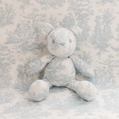 a white teddy bear sitting on top of a blue and white wallpaper covered chair