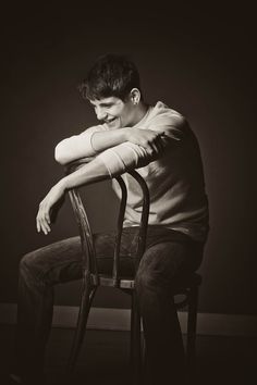 a young man sitting in a chair with his arms resting on the back of it