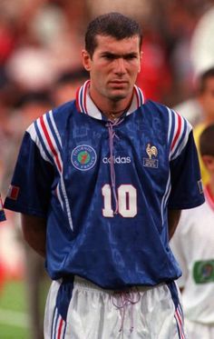 a man standing on top of a soccer field wearing a blue shirt and white shorts