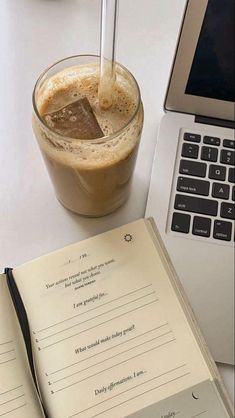 an open book sitting on top of a table next to a cup of coffee and laptop computer