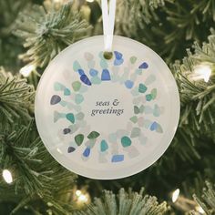 a glass ornament hanging from a christmas tree with the words seas and greetings printed on it