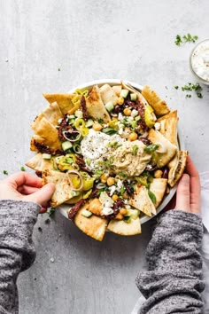 a person holding a bowl filled with food on top of a white table next to other dishes