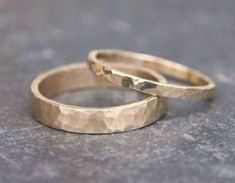 two gold wedding rings sitting on top of a gray surface, with one ring in the middle