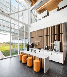 a coffee bar with orange stools in front of large windows