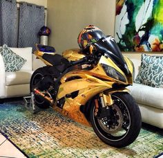 a gold motorcycle is parked in front of a white couch and colorful paintings on the wall