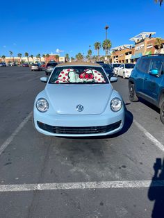 a blue vw beetle parked in a parking lot next to other cars and palm trees