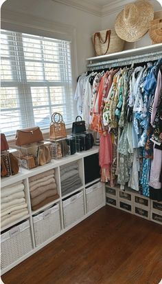 an organized closet with clothes and handbags hanging on the rack, along with baskets