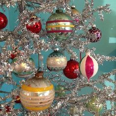 a christmas tree with ornaments hanging from it's branches in front of a blue wall