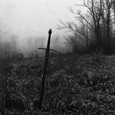 a black and white photo of a cross in the grass with foggy skies behind it