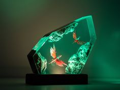 an illuminated glass sculpture with two fish in it's habitat on a black stand