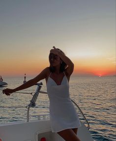 a woman in a white dress standing on the back of a boat at sunset or sunrise