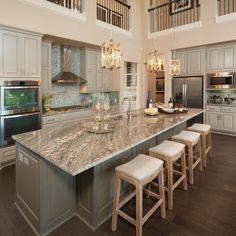 a large kitchen with an island and marble counter tops in front of stainless steel appliances