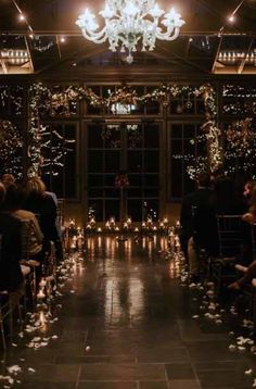 a room filled with lots of people sitting in front of a chandelier and windows