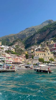 boats are parked on the water in front of some buildings and mountains with blue sky