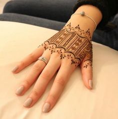 a woman's hand with henna tattoos on her left arm and fingers, sitting on a bed