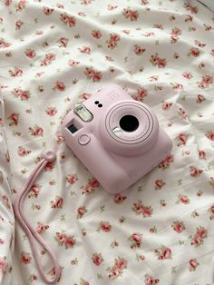 a pink camera sitting on top of a bed next to a white pillow and blanket