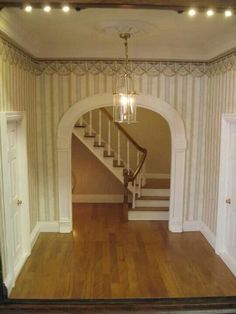 an empty living room with stairs and light fixtures on the wall, in front of a doorway