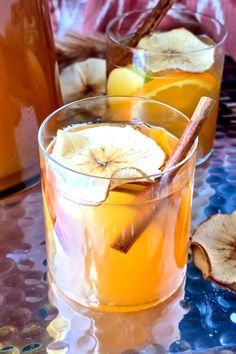 two glasses filled with apple cider on top of a table next to sliced apples