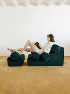 a woman sitting on top of a green couch with a book in her lap and legs crossed