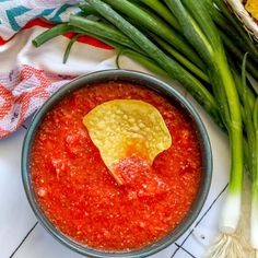 green onions and red sauce in a bowl on a white tile counter top next to garlic