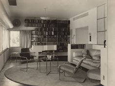 an old black and white photo of a living room with chairs, bookshelves and a couch