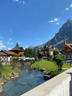 a river running through a lush green valley next to tall mountains and houses in the background