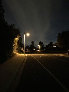 an empty street at night with the lights on and trees in the foreground,