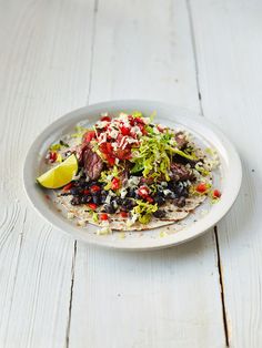 a white plate topped with lots of food on top of a wooden table next to a lemon wedge