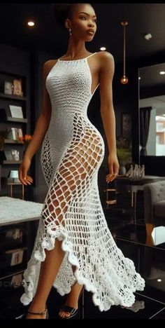 a woman wearing a white crochet dress and high heels standing in front of a table