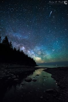 the night sky is filled with stars and milky over a body of water in front of some trees