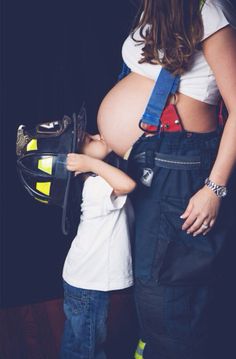 a pregnant woman and child wearing fireman's gear, standing in front of a black background