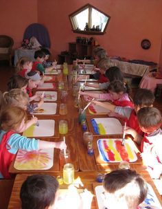 a group of children sitting at a table painting with watercolors on their plates