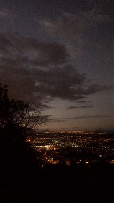 the city lights are lit up in the night sky from atop a hill at dusk