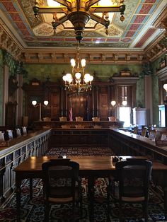 an empty courtroom with wooden tables and chairs in the center, chandelier hanging from the ceiling