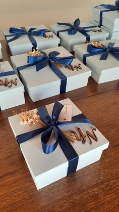 several white boxes with blue ribbons and bows on them sitting on a wooden table next to each other