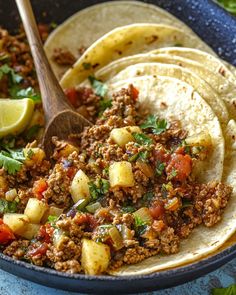 some tacos with meat and vegetables in a bowl next to a lemon wedges