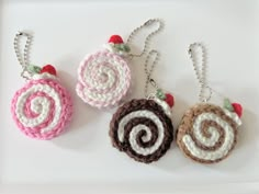 three crocheted ornaments hanging from chains on a white surface with red and green leaves