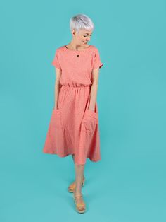 an older woman standing in front of a blue background wearing a pink polka dot dress