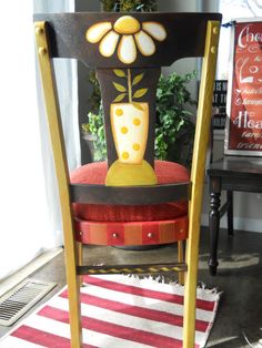 a chair with a flower painted on it sitting in front of a potted plant