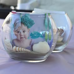 two glass bowls filled with sand and seashells on top of a purple table cloth