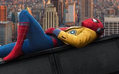 a spider man laying on top of a tall building next to a cityscape