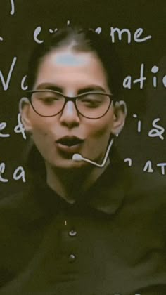 a woman wearing glasses with words written on the wall behind her and in front of her