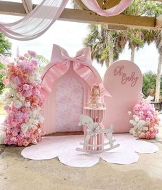 a pink and white baby's first birthday party set up with flowers, cake and rocking horse